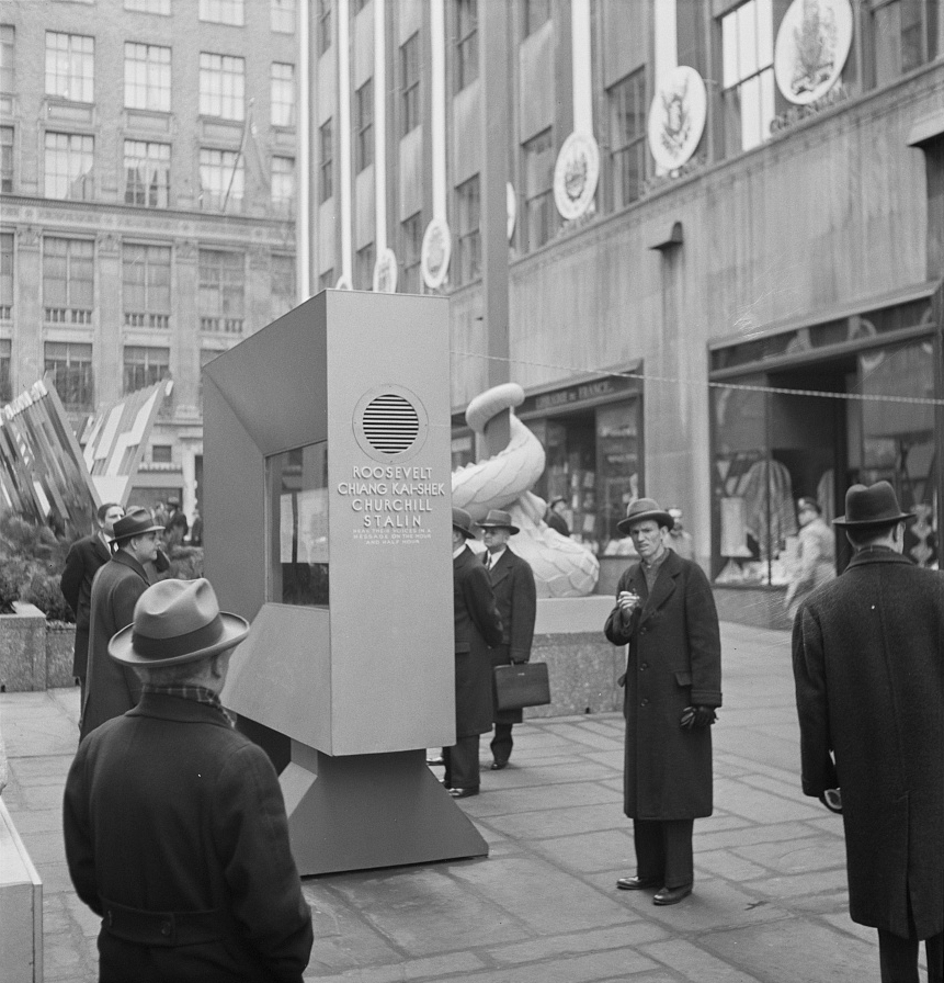 New York, New York. "United Nations" exhibition of photographs presented by the United States Office of War Information (OWI) on Rockefeller Plaza. Listening to broadcasts of President Roosevelt, Churchill, Stalin, and Chiang Kai-shek, heard every half-hour from a loudspeaker at one end of the frame containing the Atlantic charter. This frame is surrounded by four statues of the four freedoms