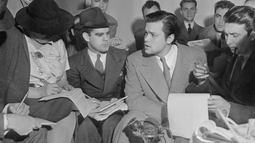 Photo of Orson Welles meeting with reporters in an effort to explain that no one connected with the War of the Worlds radio broadcast had any idea the show would cause panic. Future first Voice of America (VOA) director John Houseman was the producer of the War of the Worlds fake entertainment newscast.